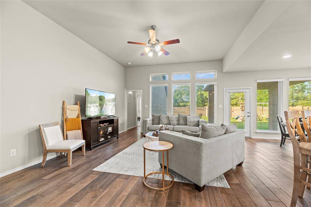 Spacious family room with wood-look tile flooring, ceiling fan and a wall of windows with backyard views.