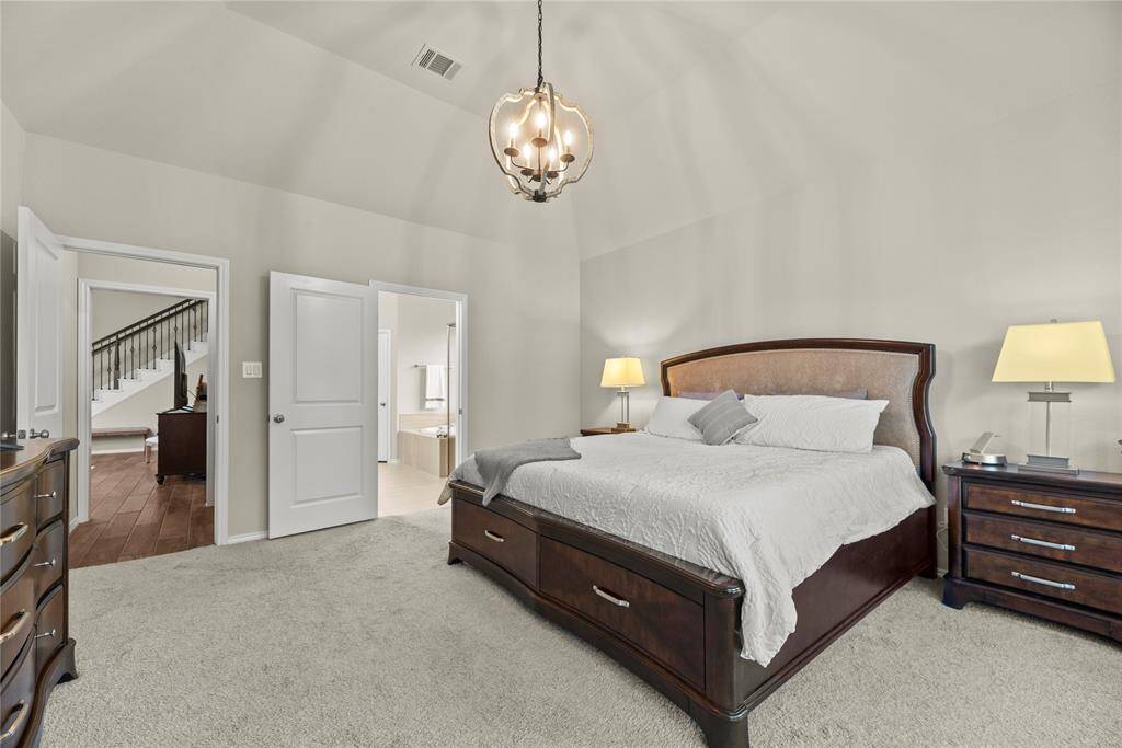The primary bedroom boasts plush carpet, high ceiling, elegant light fixture and an en-suite bathroom.