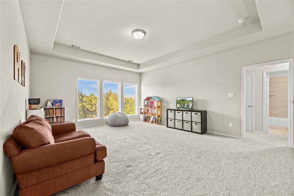 Large upstairs game room with a tray ceiling and backyard views.