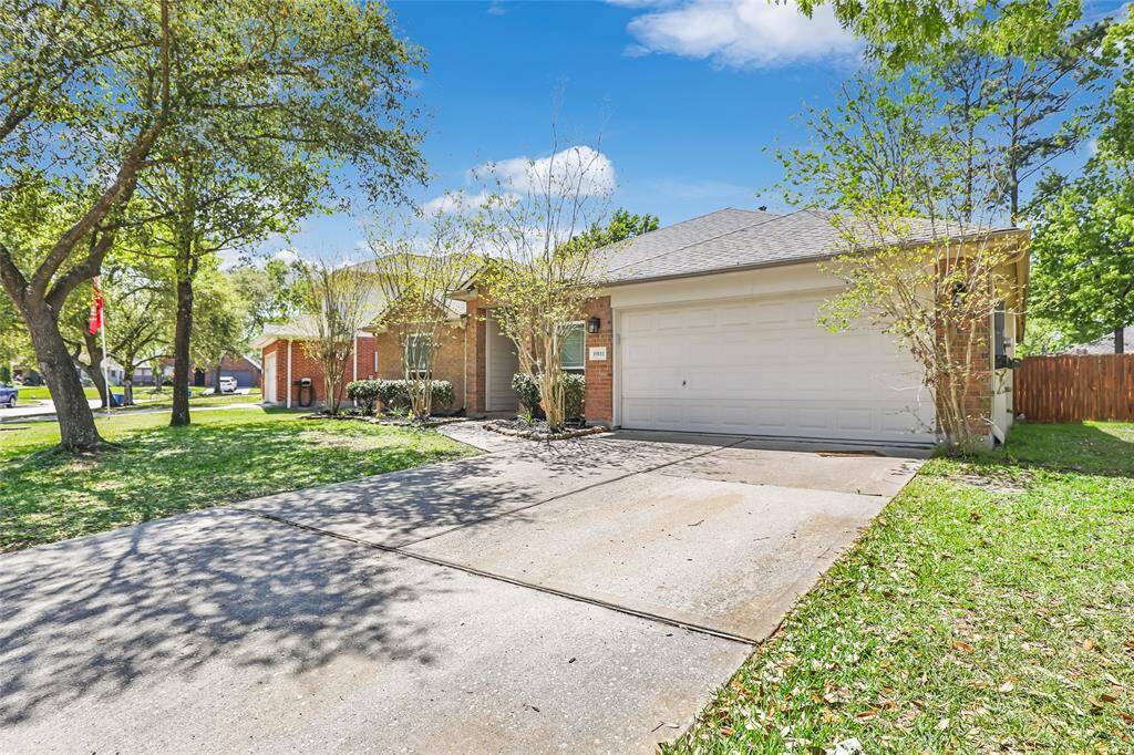 Charming single-story brick house with a two-car garage. It features a spacious driveway and a well-maintained front yard with mature trees, providing shade and curb appeal.