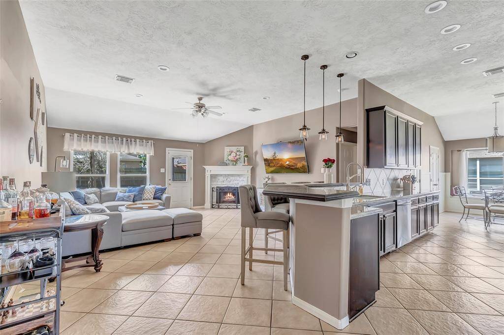 This photo showcases a spacious, open-concept living area with a modern kitchen featuring a breakfast bar, and pendant lighting. The living room has a cozy fireplace, and plenty of natural light from the windows. The dining area is adjacent, creating a seamless flow for entertaining.