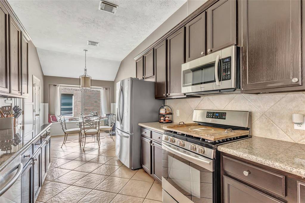 This kitchen features stainless steel appliances, granite countertops tons of storage and counter space. The space is brightened by a large window in the dining area, with tile flooring extending throughout. A cozy dining nook offers an inviting spot for meals.