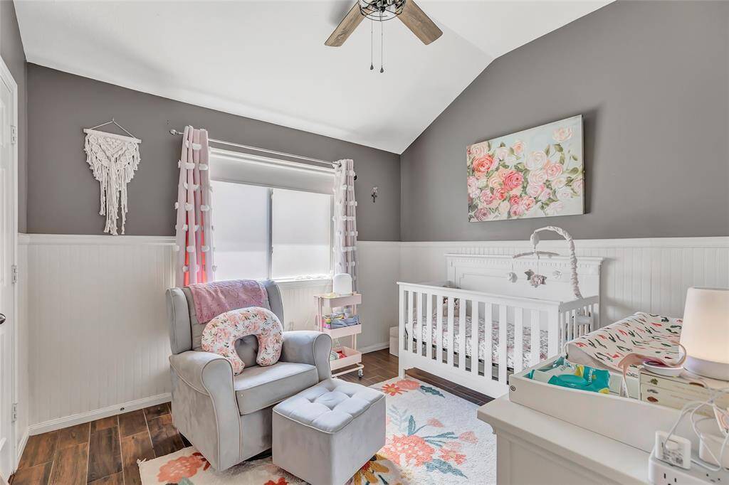This photo features a cozy nursery with a soft color palette. The walls are painted in a soothing neutrals with wainscoting. Natural light fills the room, offering a wonderful place to rest and relax, read books and enjoy time with little ones.