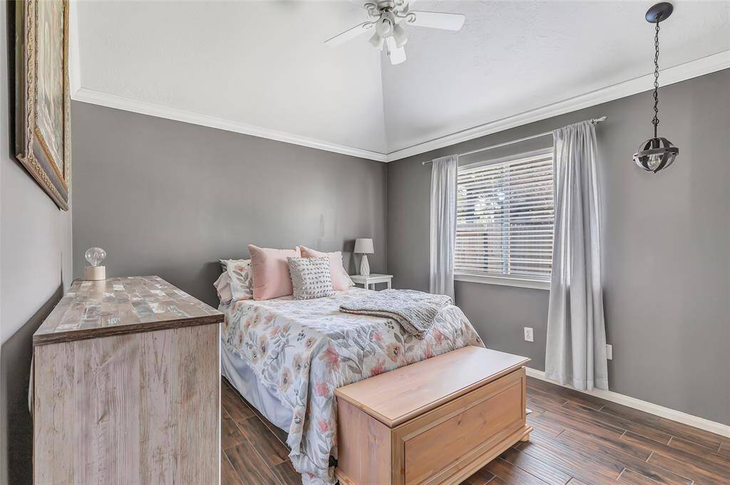 This spacious guest bedroom features a vaulted ceiling with a fan, a large window, and a soft color palette. Wonderful space for family and friends to retreat.