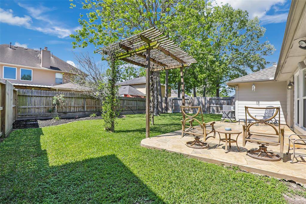 Elegant backyard patio featuring wooden pergola. The space is framed by a well-maintained lawn and surrounded by a wooden fence, offering privacy and a great spot for relaxation or entertaining.