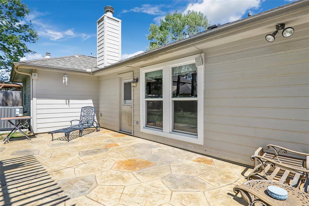 Spacious and sunny backyard patio with stone flooring, perfect for outdoor relaxation and entertaining. The area features ample space for seating and is adjacent to a well-maintained exterior wall with large windows, providing a seamless indoor-outdoor flow.