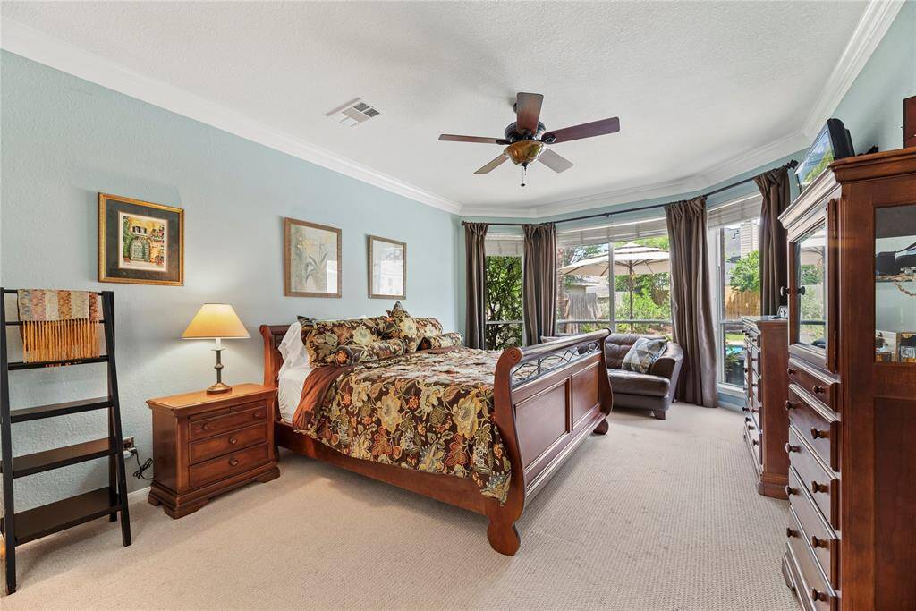 First-floor primary bedroom measuring 12.7 x 18.6, featuring carpet flooring, a ceiling fan, and large windows with serene views of the backyard.