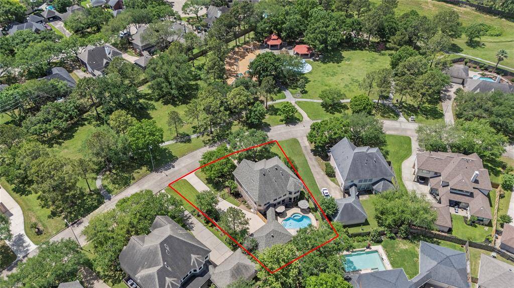 Aerial view of the neighborhood showcasing the peaceful, tree-lined streets, nearby community park, and the home’s prime location on a spacious pie-shaped lot directly across from playground and splash pad amenities
