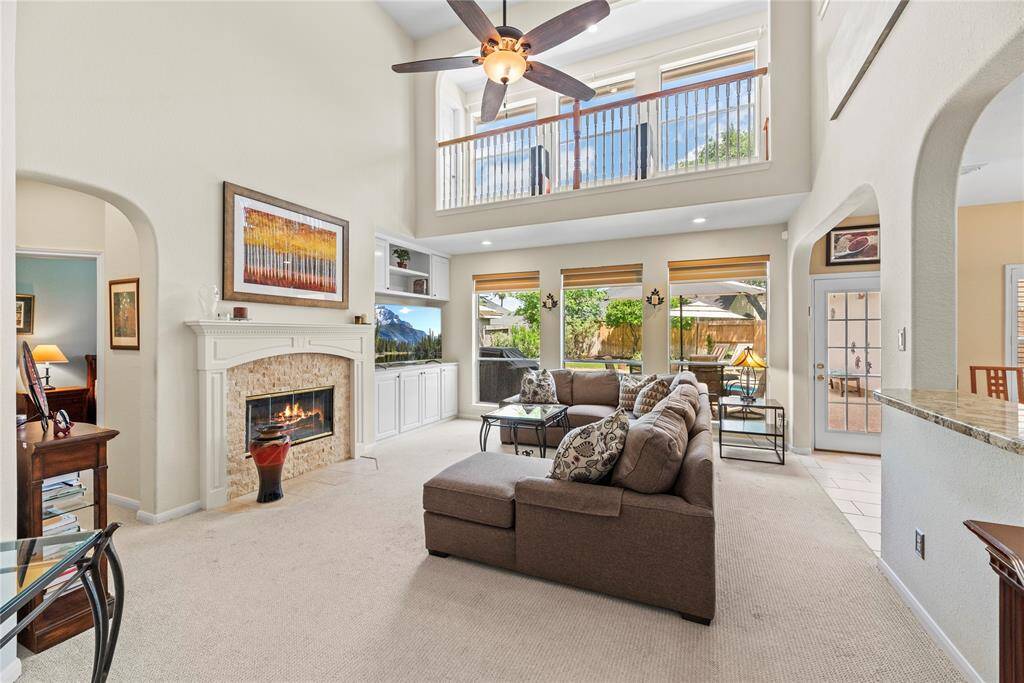 Spacious family room measuring 17.8 x 24.5 features carpet flooring, a ceiling fan, a fireplace, and large windows overlooking the backyard. The open kitchen sits to the right, separated by a convenient bar-height counter. A second-floor balcony overlooks the space, adding an open and airy feel.