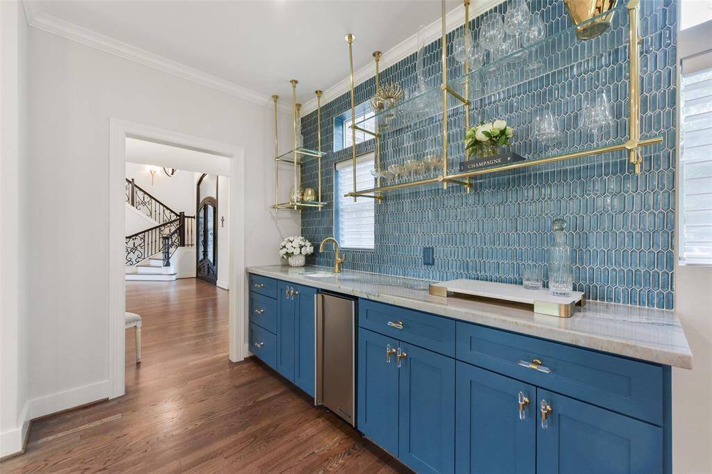 Wet bar with custom hanging brass and glass shelving, high end decorative tile, and coordinating pulls. Hoshizaki ice machine at bar perfect for serving.