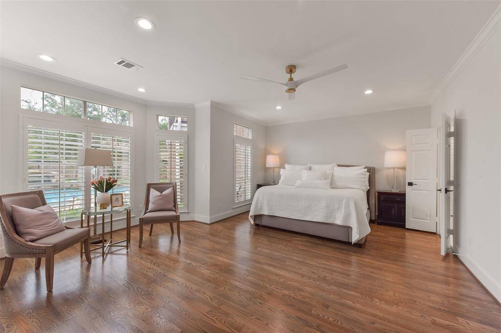 Large primary suite has wood flooring, modern lighting, a wall of windows overlooking the pool, natural light, plus plenty of space for a sitting area.