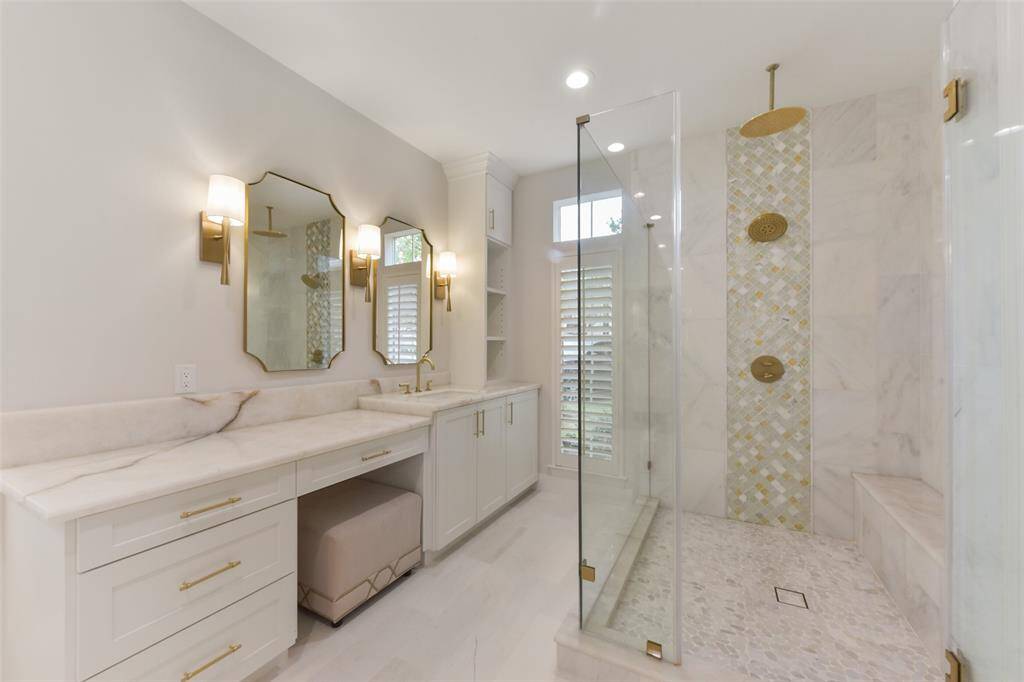 Custom glass walk-in shower features dual shower heads, updated brass hardware, rain shower, and designer tile.