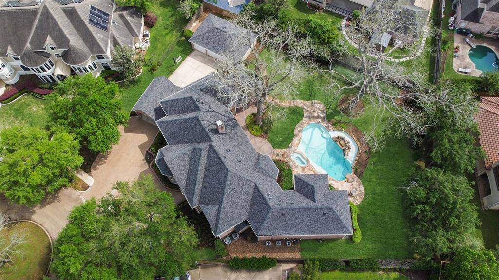 The aerial view showcases the almost 1/2 acre property including mature trees, pool, spa, 3 car garage, and batting cage.