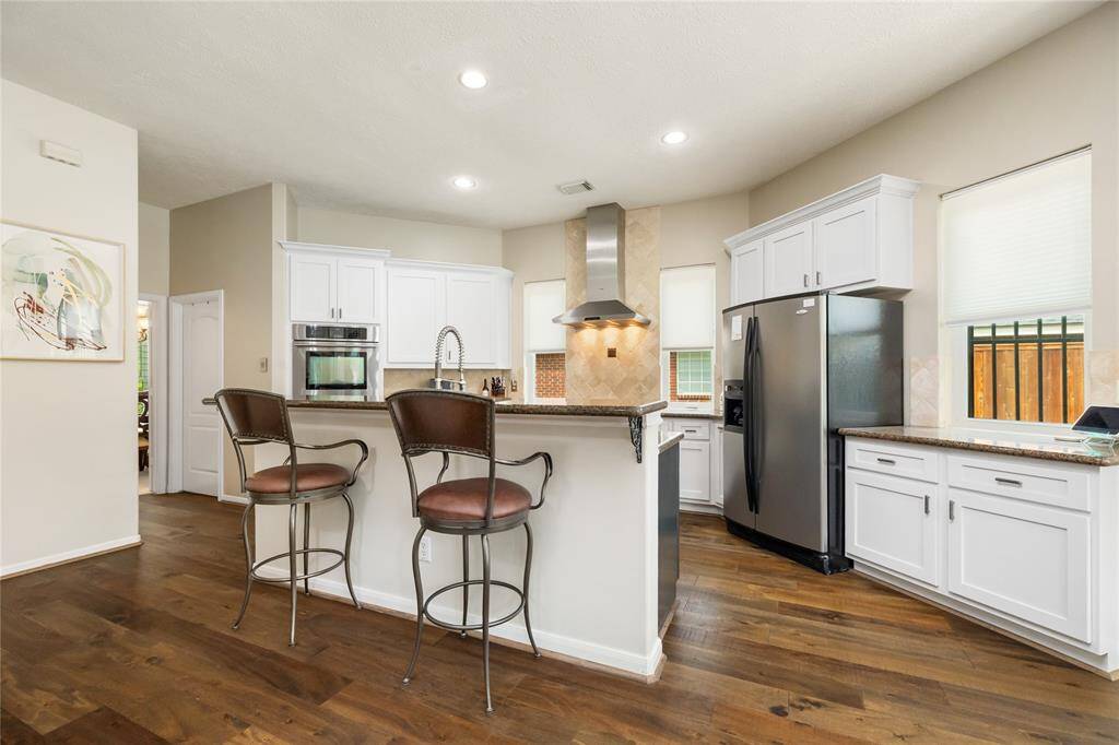 From the living area, this bright and modern kitchen is designed for both style and functionality. Featuring stainless steel appliances, white cabinetry, and hardwood floors, the central island with bar seating creates a seamless connection between cooking and casual dining.