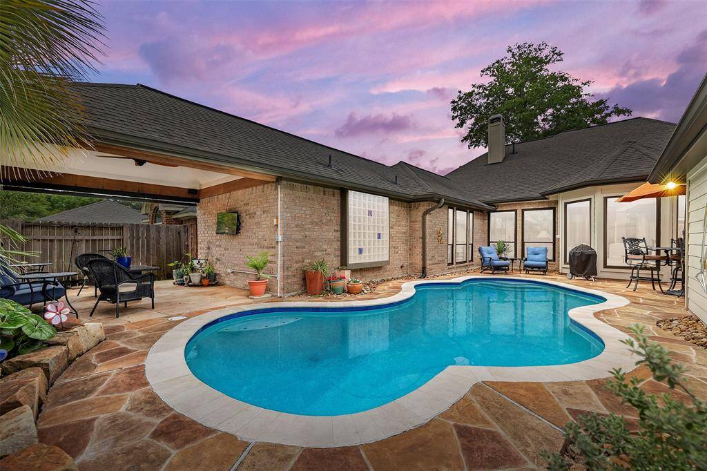 Step into your own private oasis—this serene backyard is highlighted by a sparkling pool, bordered by a stone patio. A cozy, covered seating area invites you to unwind, while lush greenery and a vibrant sunset sky complete the tranquil atmosphere, perfect for both relaxation and entertaining.