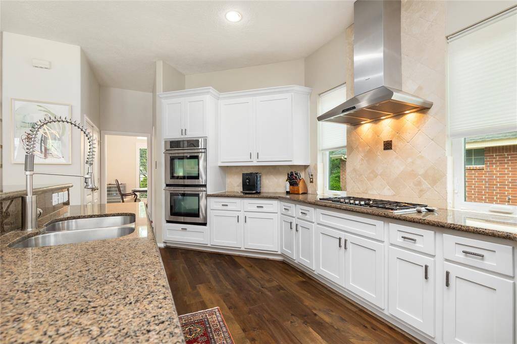 This well-appointed kitchen showcases modern white cabinetry, sleek granite countertops, and top-of-the-line stainless steel appliances, including a double oven and gas cooktop.