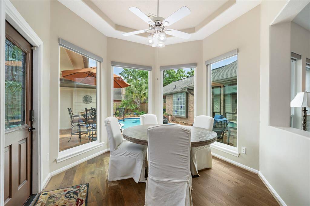This bright and inviting breakfast nook offers stunning views of the backyard pool and patio area through large windows. The space is bathed in natural light, with wood flooring adding warmth and a ceiling fan for added comfort—perfect for enjoying morning meals or casual moments throughout the day.
