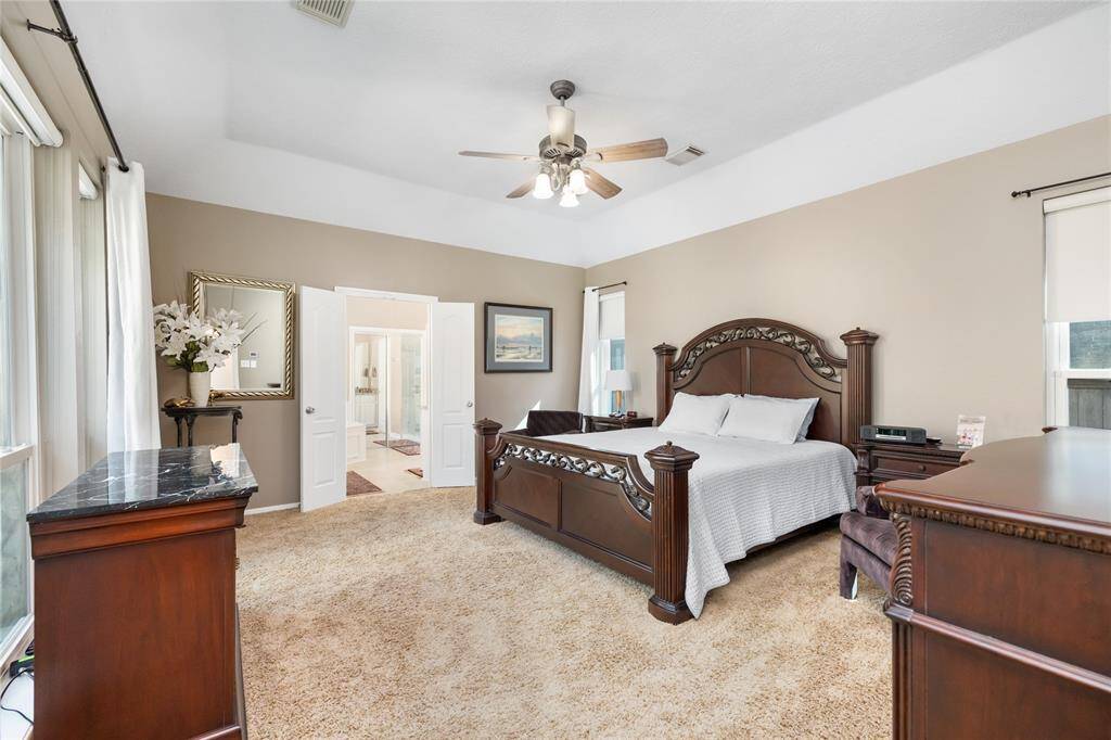 This spacious primary bedroom is a serene retreat, with large windows that flood the room with natural light. French doors open to the luxurious ensuite bathroom, creating a seamless flow between spaces. The room’s neutral tones and plush carpeting enhance the peaceful, restful atmosphere.