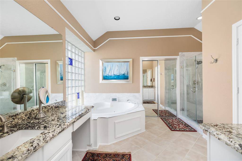 This spa-inspired en-suite offers a spacious layout with dual granite vanities, a corner jacuzzi tub, and a glass-enclosed shower. (Shower, Tub, & Tile Updated in 2024!) Neutral tones and large mirrors reflect natural light, creating a bright, airy atmosphere that feels both elegant and relaxing.