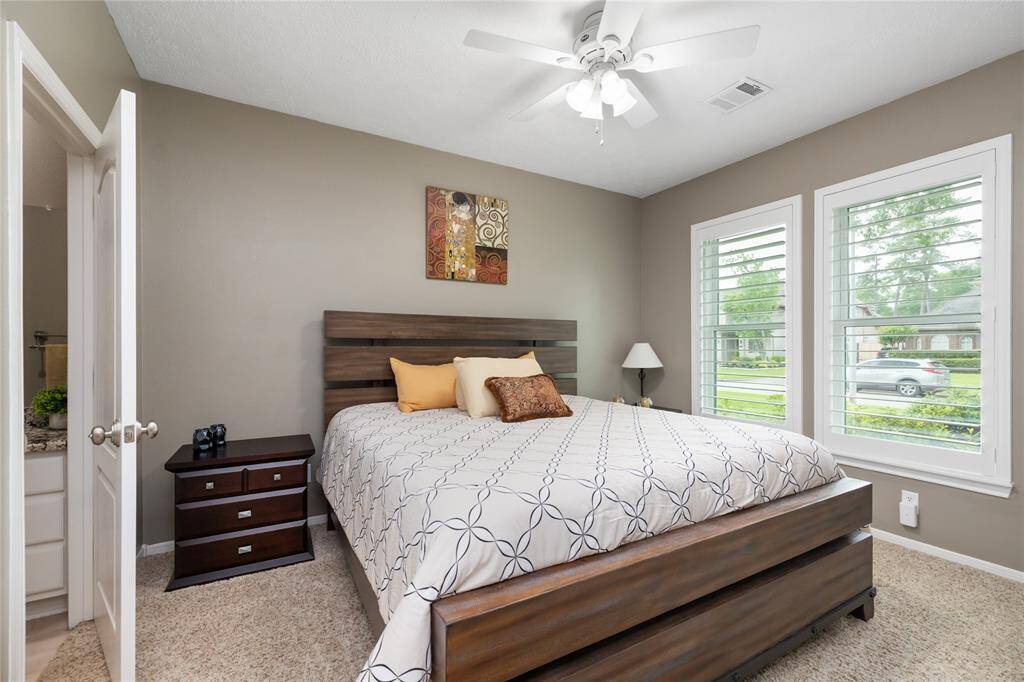 This cozy secondary bedroom offers a peaceful retreat with soft carpeting, neutral tones, and abundant natural light from dual windows, and a ceiling fan enhances year-round comfort.