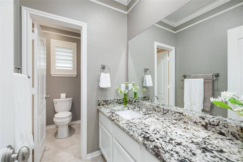 This stylish Jack & Jill bathroom features dual sinks with a sleek granite countertop and white cabinetry, offering both elegance and functionality. Crown molding, a large mirror, and soft gray tones create a calm, polished feel—perfect for shared use without sacrificing privacy.