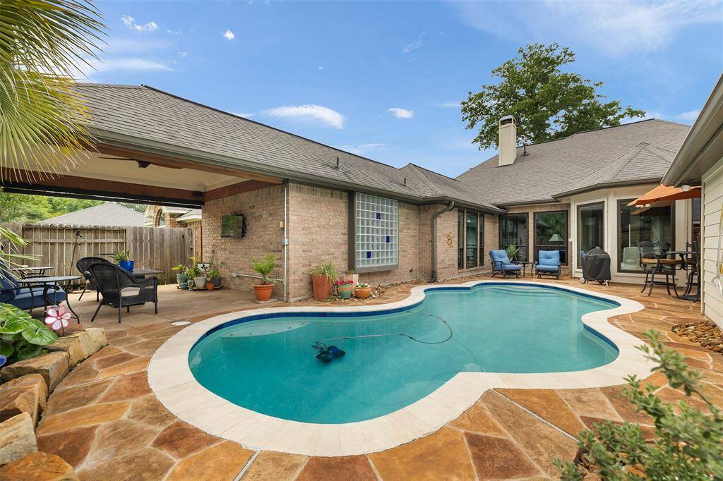 This backyard oasis features a freeform swimming pool surrounded by a flagstone patio, offering a perfect blend of relaxation and entertainment. Ample seating, potted plants, and a covered area for shade create a serene outdoor retreat. The home's brick and glass exterior adds a stylish touch, enhancing the inviting atmosphere of this outdoor living space.