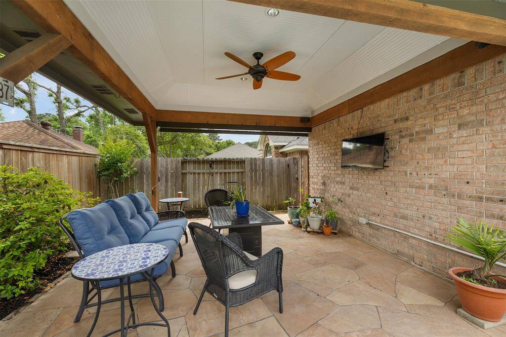This covered patio is an ideal setting for creating lasting memories, with a ceiling fan for comfort and a mounted TV for entertainment. The stone flooring and brick wall provide a cozy, inviting atmosphere, while the surrounding greenery adds a touch of tranquility—perfect for enjoying relaxed moments with family and friends.