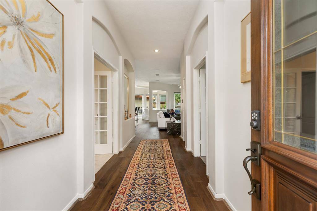 Step through the front door into a warmly lit entryway, where elegant wood flooring set the stage for the home’s inviting atmosphere. The hallway flows into a spacious, open living area, offering a glimpse of the bright, welcoming interior that promises comfort and tranquility.