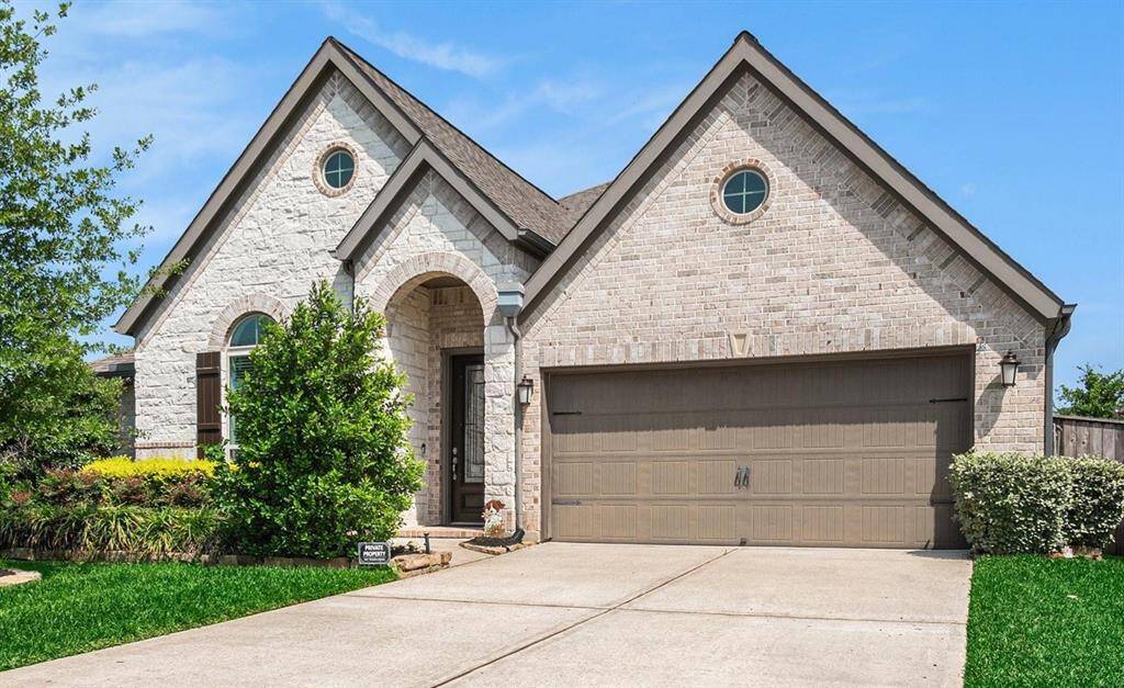 Charming single-story brick and stone exterior. The front yard features well-maintained landscaping with lush greenery and a welcoming arched entryway