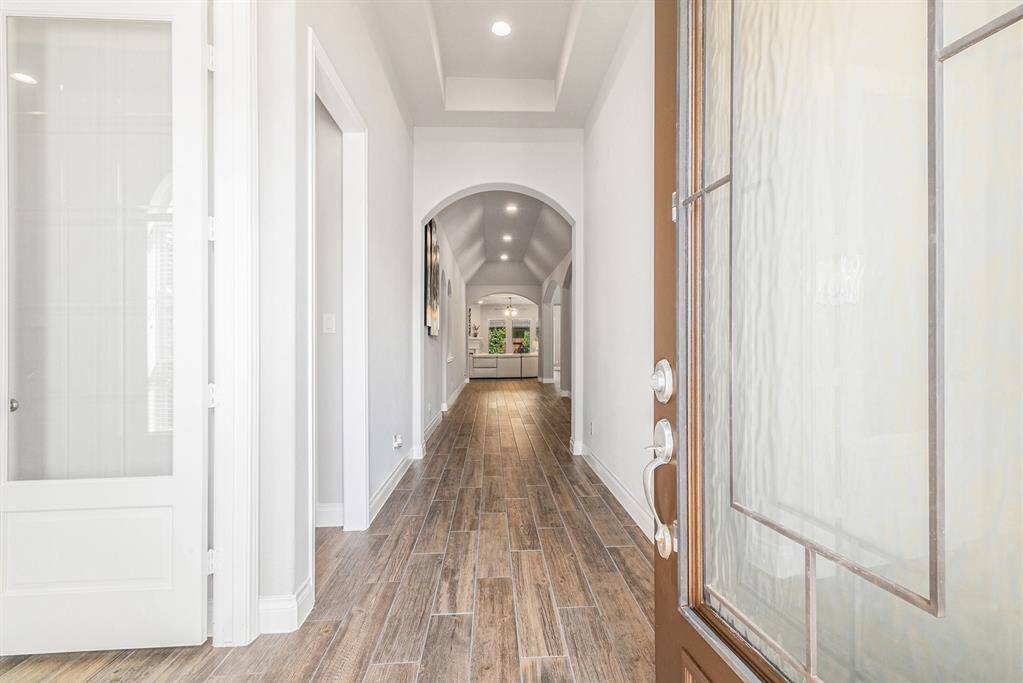 Bright entryway with elegant arched openings and wood-look tile flooring. It features a modern glass front door and neutral wall colors, creating a welcoming and spacious feel.