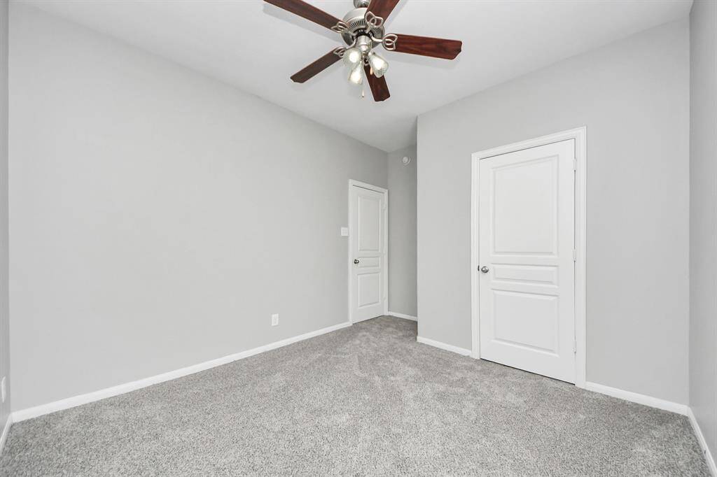 This room features soft gray walls and plush carpeting, offering a cozy atmosphere. It includes a ceiling fan for comfort, and two white doors that lead to a closet and an additional space.