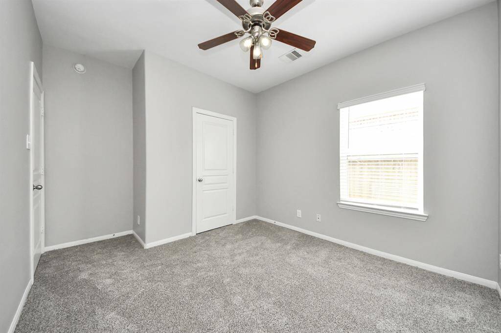 This photo showcases a cozy, carpeted bedroom with soft gray walls and a ceiling fan. It features a window for natural light and a door leading to a closet.
