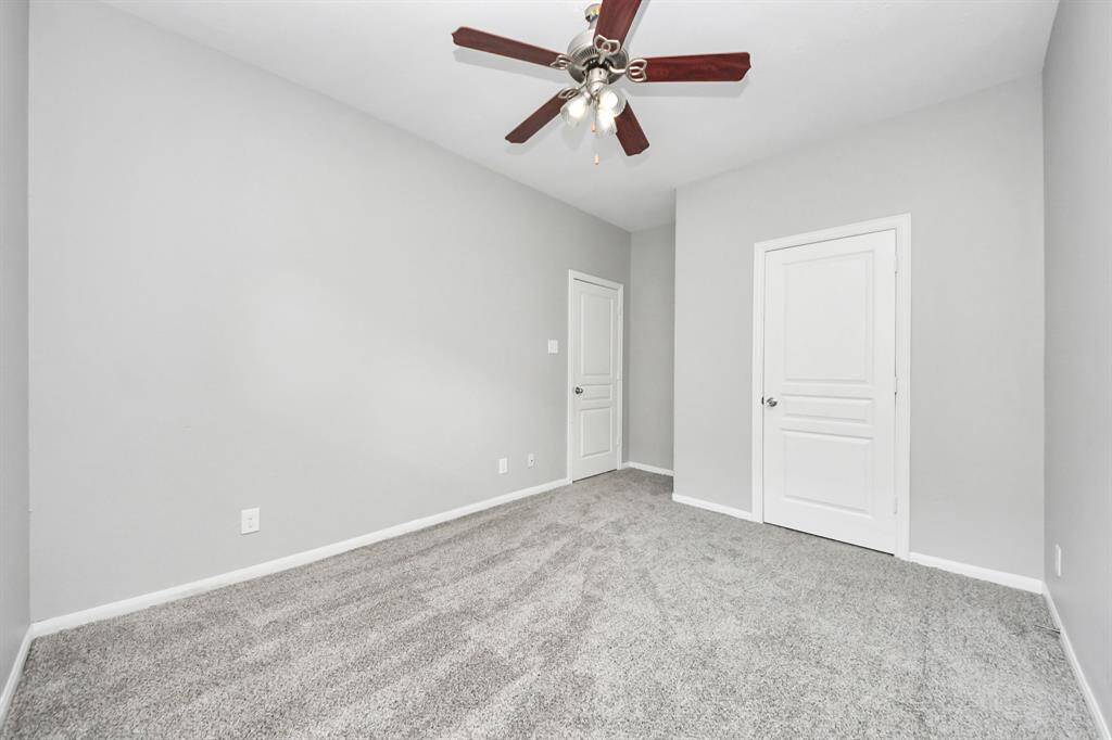 A cozy room with soft gray carpeting and light gray walls, featuring a ceiling fan and two white doors, ideal for a bedroom or office space.