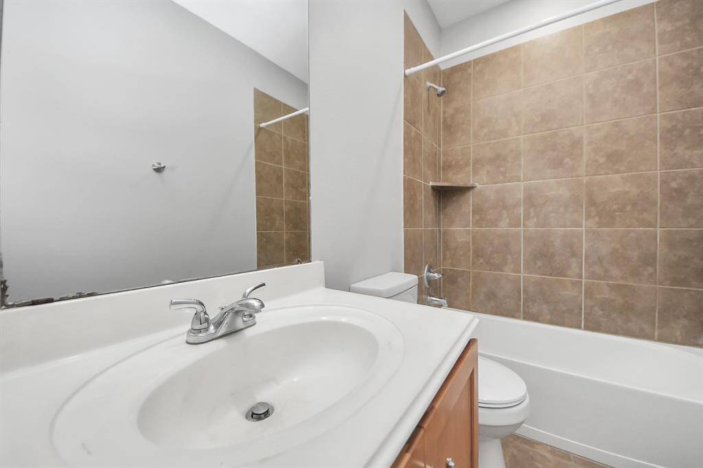 This bathroom features a modern design with a white vanity and sink, chrome fixtures, and a shower-tub combo surrounded by beige tiles, providing a clean and functional space.