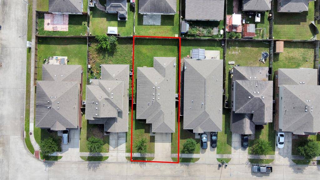 This aerial photo shows a suburban home outlined in red, featuring a rectangular backyard. It's situated in a neighborhood with similar houses, offering a neat driveway and a fenced yard for privacy.