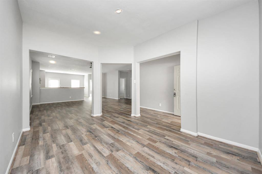 This photo shows a spacious, open-concept living area with light gray walls and wood-style flooring, offering ample natural light through large windows. The layout provides easy access to adjoining rooms, making it ideal for family living and entertaining.