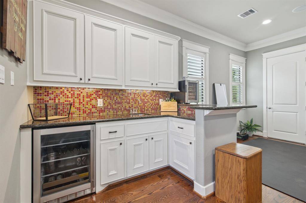 The bar area is both stylish and functional, featuring a chic tile backsplash and a built-in wine or beverage refrigerator. Whether you're hosting guests or enjoying a quiet evening in, this space is perfect for serving drinks and showcasing your favorite selections with flair.
