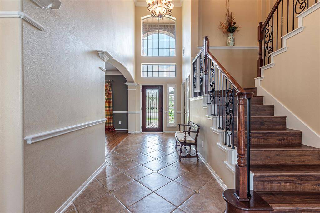Spacious entryway with tile flooring, ceilings spanning two levels, hanging light fixture and glass panel front door.