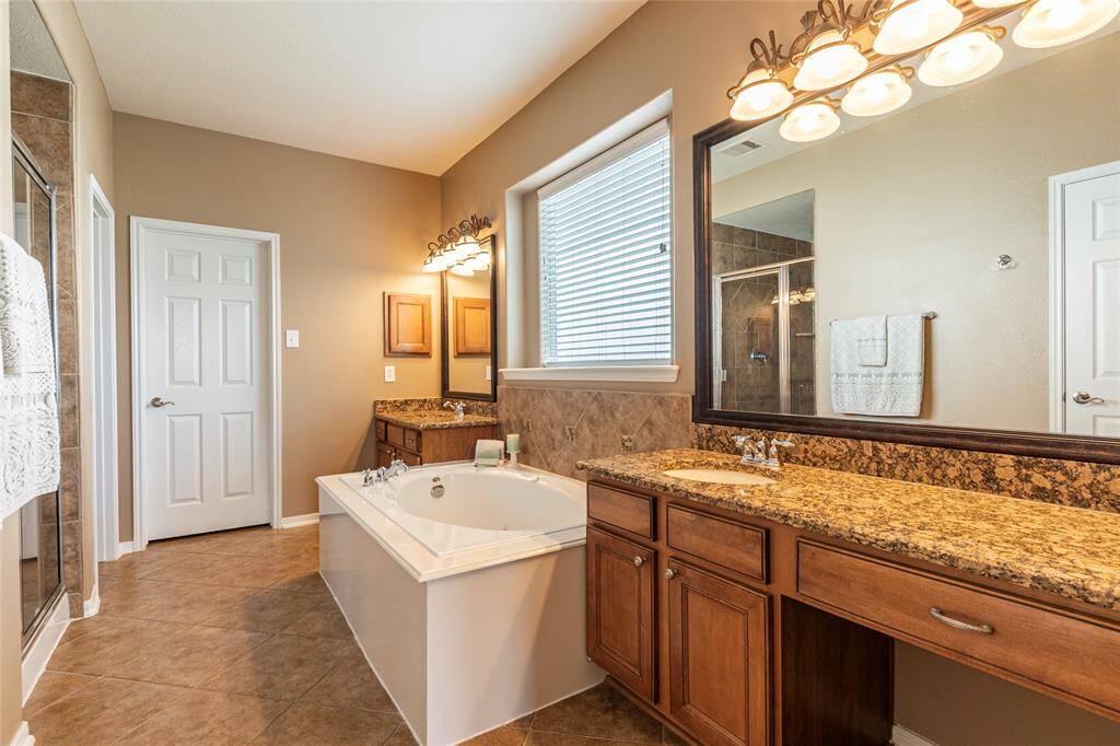 Beautiful primary bath with tile flooring, dual vanities, granite counter tops and separate jetted tub and walk in shower.