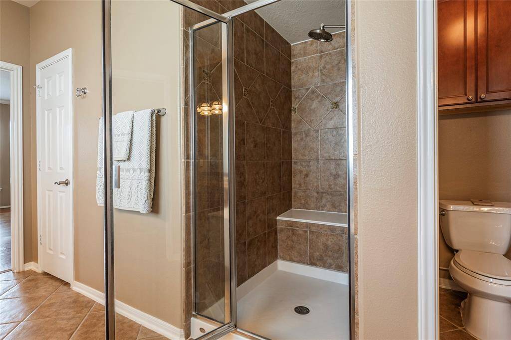 Walk-in glass door shower with seating bench and ceramic tile surrounding. Linen closet to the left and storage cabinet in the water closet.