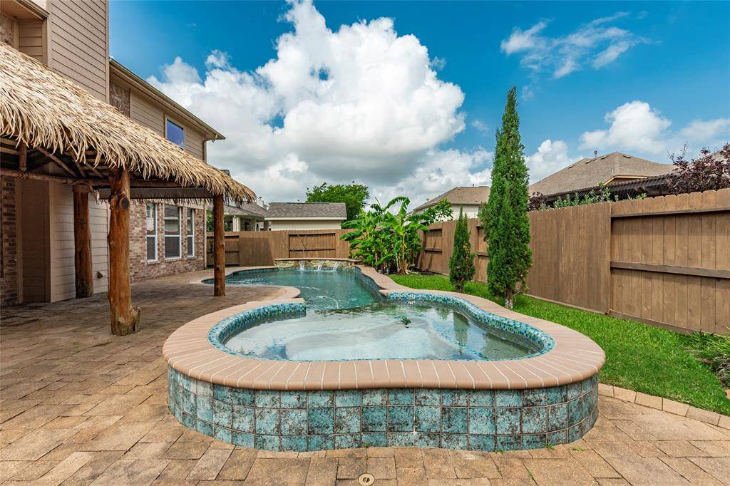 Tropical backyard with coastal blue tile accent surrounding the hot tub with spillover into the pool.