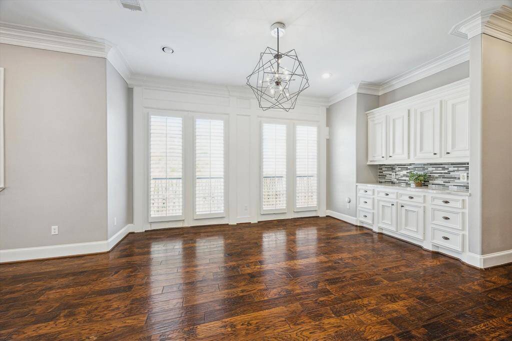 The dining area is centered around a designer chandelier and framed by floor-to-ceiling windows, dressed with plantation shutters that invite an abundance of natural light. For extra storage, the room includes a built-in buffet for extra storage.