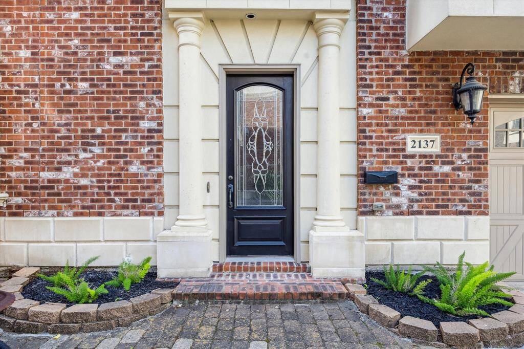 Brick-paved front steps lead to an elegant entryway, beautifully framed by a decorative door and architectural stone detailing, creating a grand and inviting first impression.