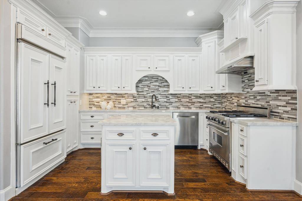The kitchen boasts elegant marble countertops, dual sinks with a pull-down faucet, and a decorative backsplash. The custom cabinetry is complemented by a cabinet-front built-in KitchenAid refrigerator and Bosch dishwasher.