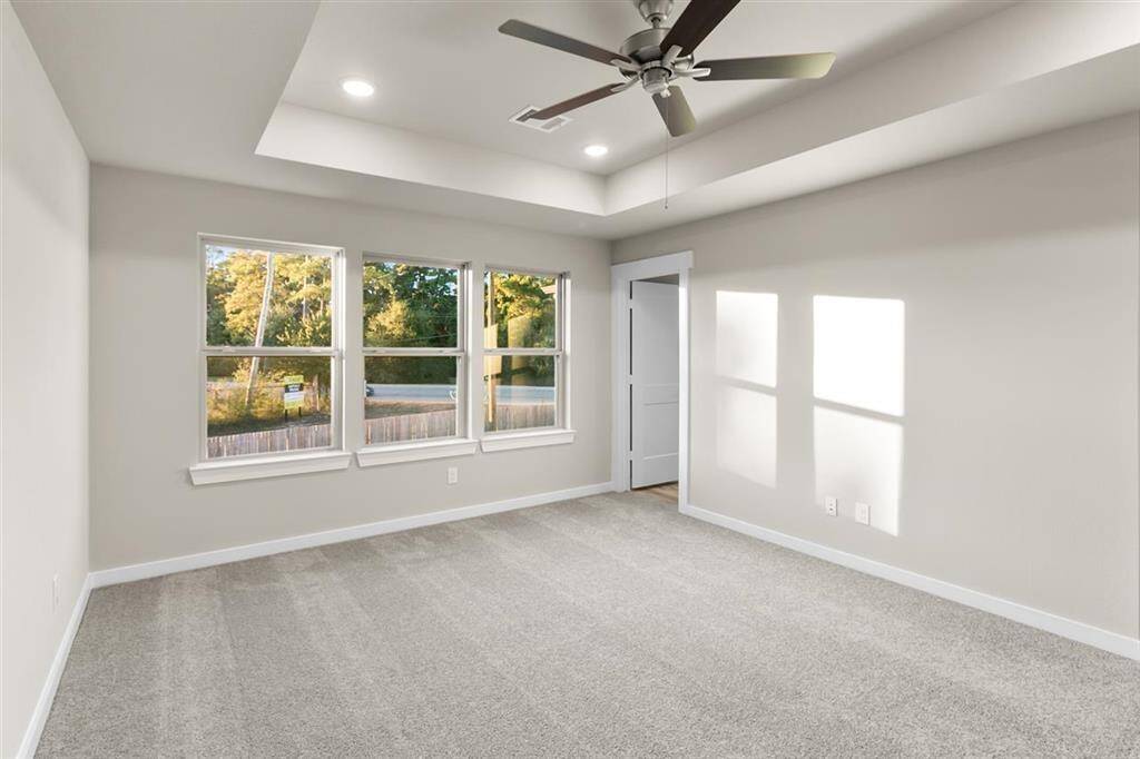 As you enter the primary bedroom, you’re greeted by an abundance of natural light pouring in through large, beautifully framed windows, casting a warm glow on the soft, neutral tones of the walls.