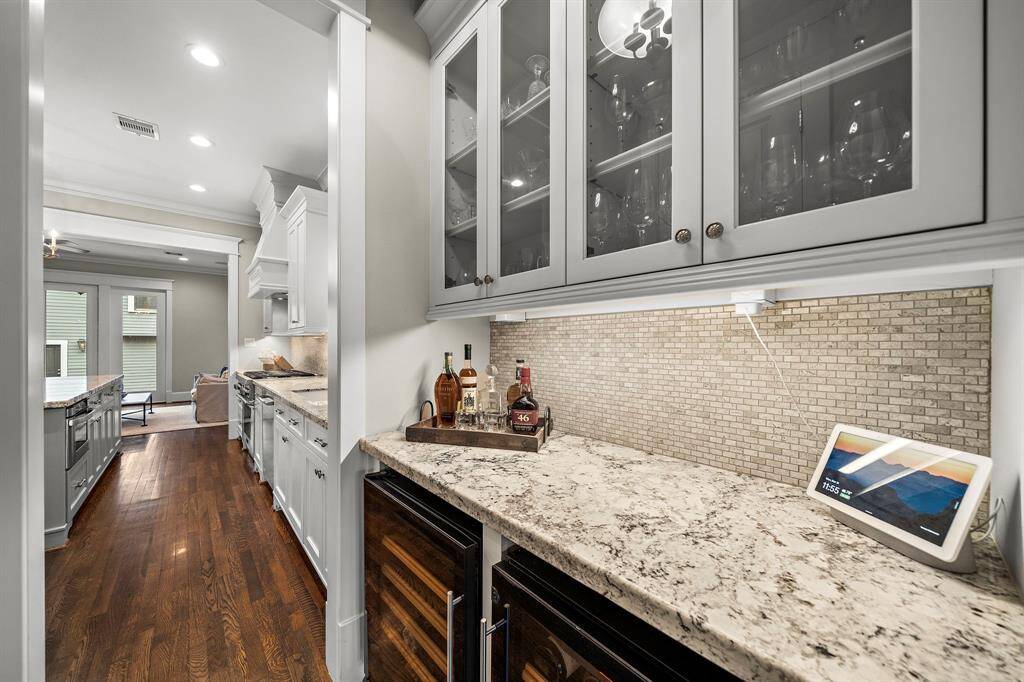 The bar off the kitchen features granite countertops, a stunning backsplash, space for two wine refrigerators, and ample cabinet storage—perfect for mixing drinks and storing your favorites! Just across from this, you'll find a convenient walk-in pantry for all your storage needs.