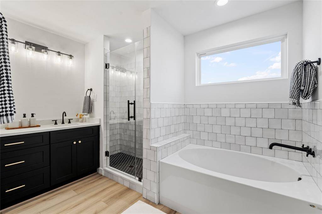 This luxurious primary bathroom features a sleek built-in tub and a spacious walk-in shower, offering a spa-like experience at home. The elegant quartz countertops complement the modern design, while the large window fills the space with natural light, creating a bright and serene atmosphere.