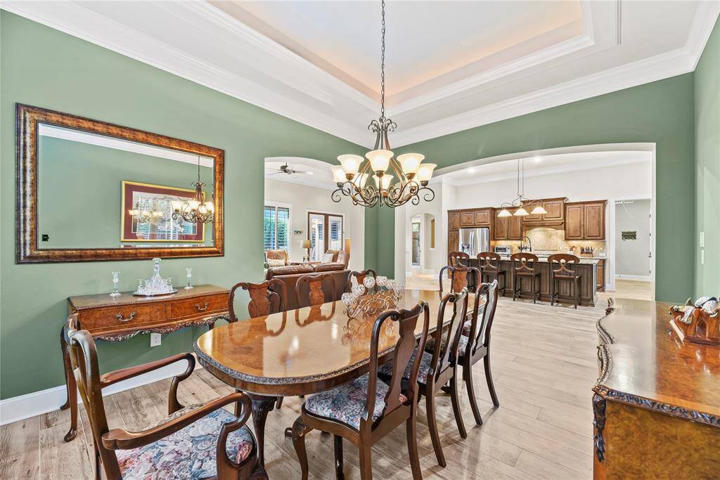 Formal dining room offers a tray ceiling, crown molding, wood-look tile flooring and an elegant light fixture.