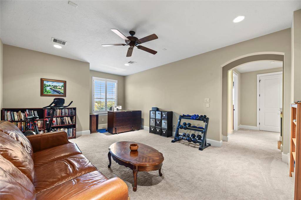 Versatile upstairs game room with plush carpet and a ceiling fan.