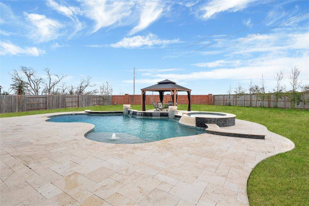 This backyard is an outdoor oasis. It features a spacious swimming pool with a hot tub, surrounded by travetine decking. A stylish gazebo offers a shaded seating area, and the entire space is enclosed by a privacy fence.